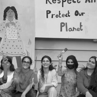 Photo of an activity by Gender Interactive Alliance (GIA) where people are holding up paint brushes after painting a mural