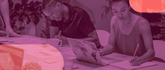 Consultancy to conduct a Mid-Term Review of AWID’s Strategic Plan. It shows two coworkers sharing a table while doing individual work. To the left is a black man with braids and to the right is a woman of east asian descent.